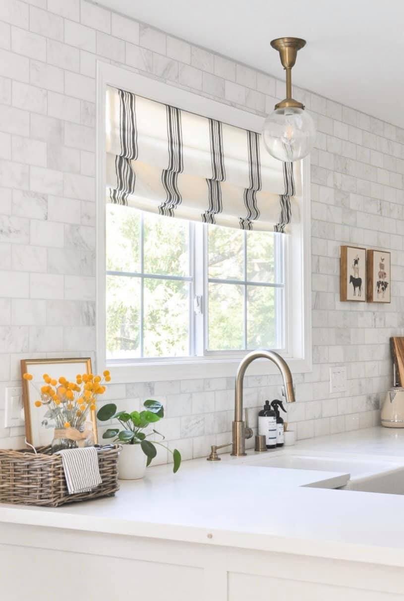 Relaxed roman shade with bold horizontal stripes in a kitchen with white subway tile backsplash and brass pendant light