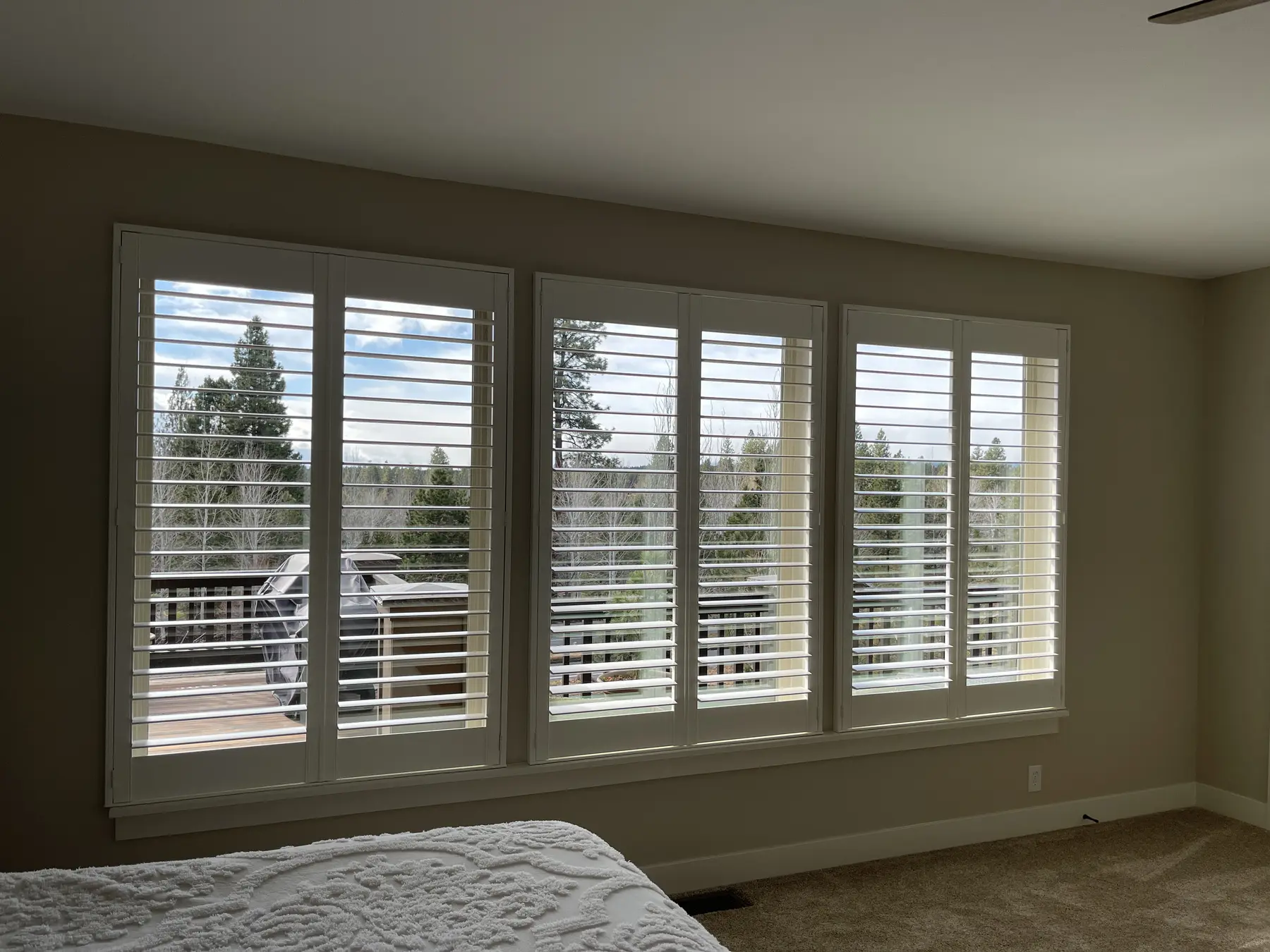 White plantation shutters across a primary bedroom window wall