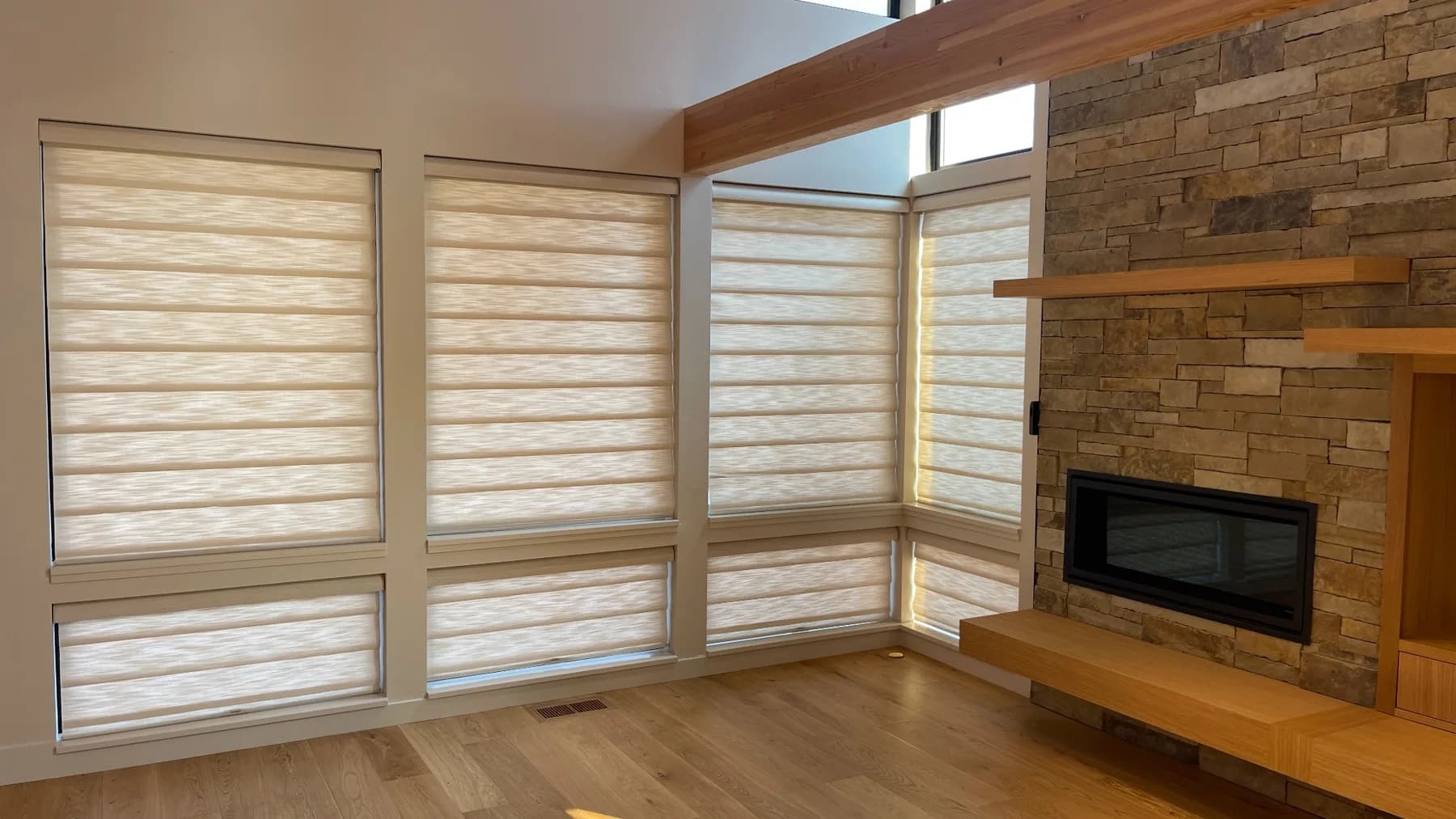 Hunter Douglas fabric shades along a window wall beside a stone fireplace
