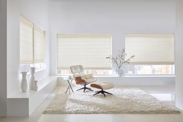 Large woven roller shades in a bright minimalist white living room, demonstrating clean flat installation without puckering