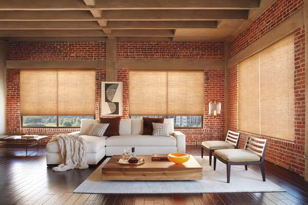 Natural woven wood Roman shades in a warm rustic living room with exposed brick walls and hardwood floors